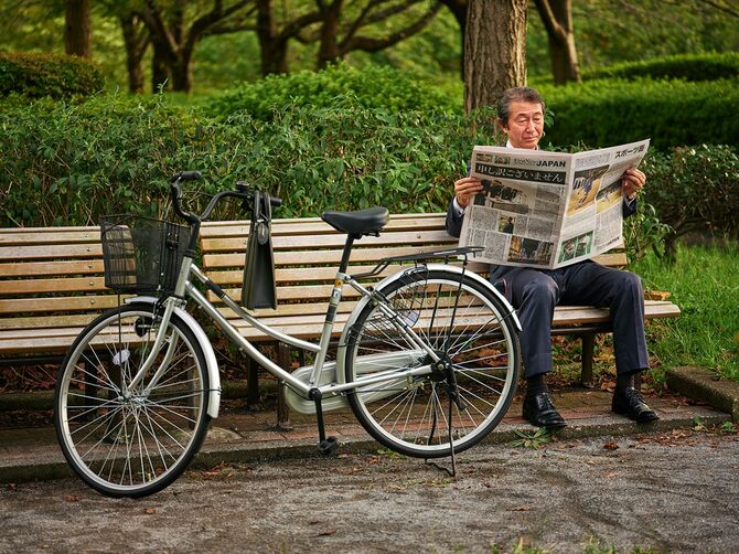 公園のベンチで新聞を読む男性