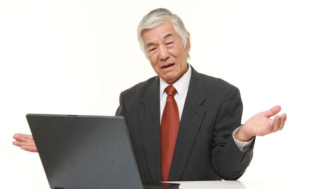 ノートパソコンを前にちんぷんかんぷんだと両手を広げるシニアのビジネスマン
