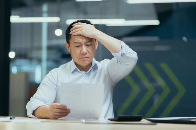 頭を抱え、心配そうに書類を見ている男性