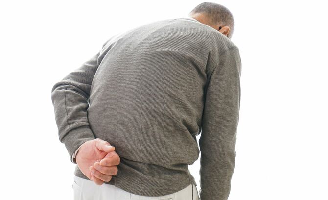 腰の痛みを感じている、腰の曲がったシニア男性