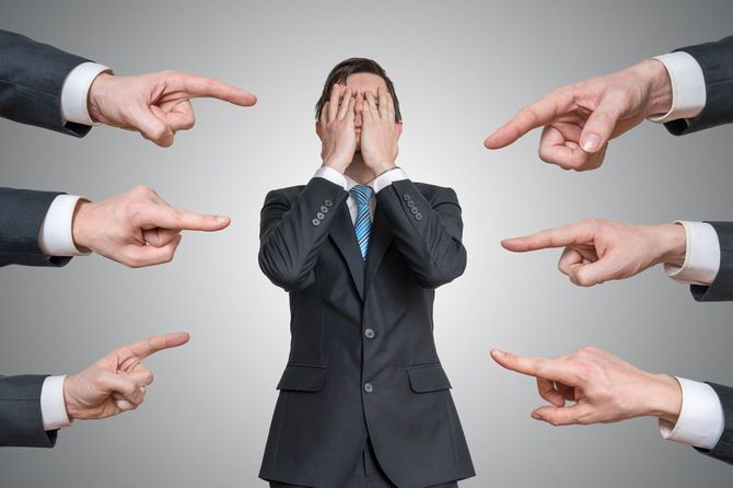 多くの手に指さされて顔を隠している男性