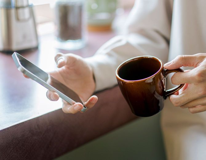 コーヒーカップとスマートフォンを持つ人の手のクローズアップ
