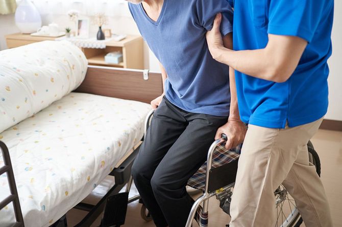 ベッドから車椅子へ移動する高齢者を助ける介護者