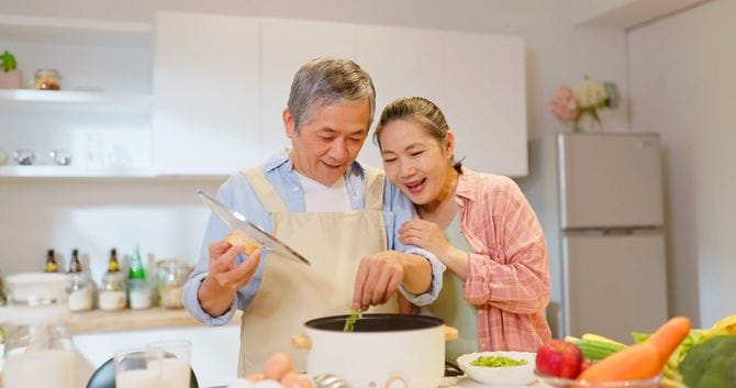 シニアカップルが、キッチンで寄り添いながら調理中