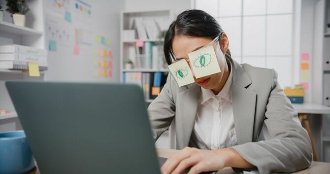 デスクで隠れて居眠りをするビジネスウーマン