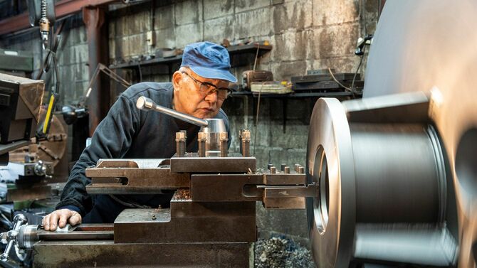 下町の鉄工所で旋盤を操作するシニア男性の社長