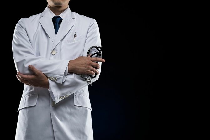 黒い背景に立つ、腕を組んでいる男性医師