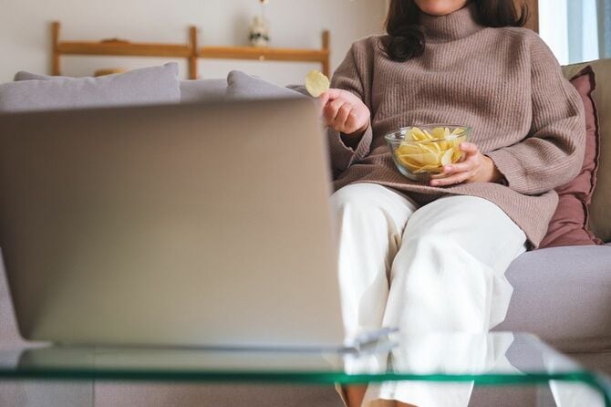 ラップトップコンピュータで映画を見ながらポテトチップスを食べる女性