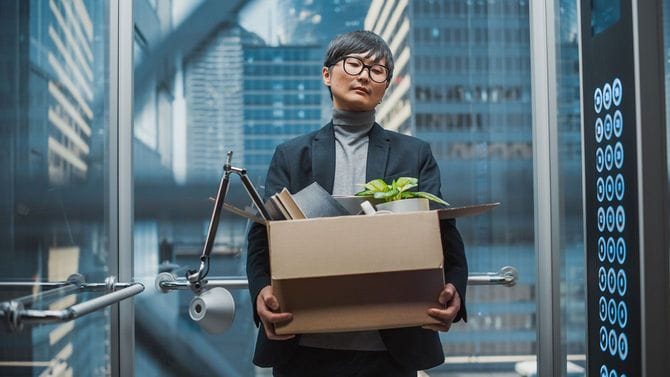 段ボールに入った荷物を持ちオフィスのエレベーターに乗っている男性