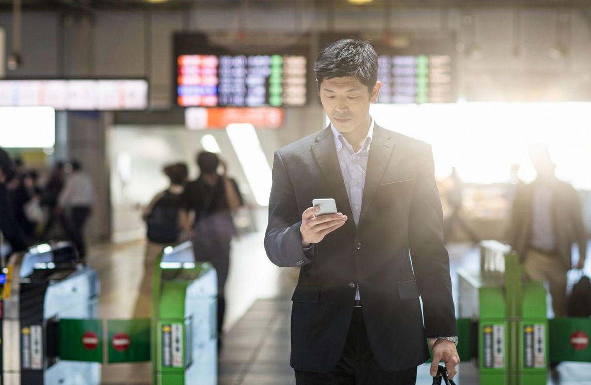 駅で携帯電話をチェックする日本人ビジネスマン