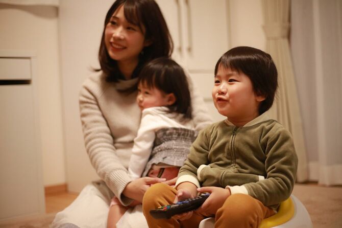 テレビのリモコンを握る男の子と娘をだっこしてほほ笑む母親