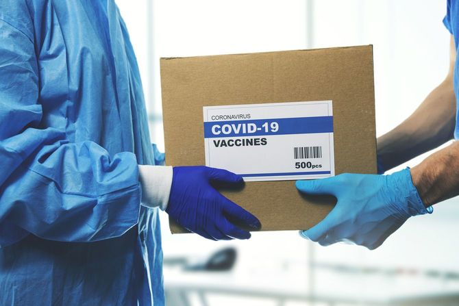 新型コロナのワクチンと書かれたシールが貼ってある段ボールを受け取る医療従事者