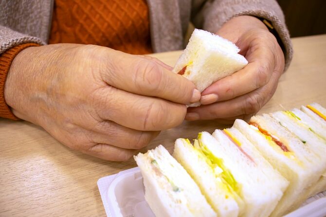 小さなサンドイッチの一切れめを手に持っているシニア女性