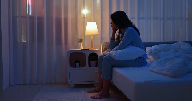 ベッドに座って窓の外を眺める女性