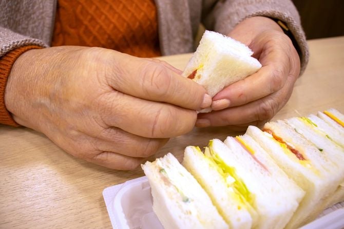 小さなサンドイッチの一切れめを手に持っているシニア女性