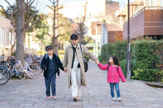 働く母親が娘たちと手をつないで一緒に通りを歩いている
