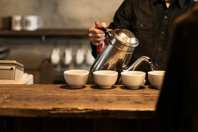 カフェで働く男性バリスタがカップにお湯を張り、温めている