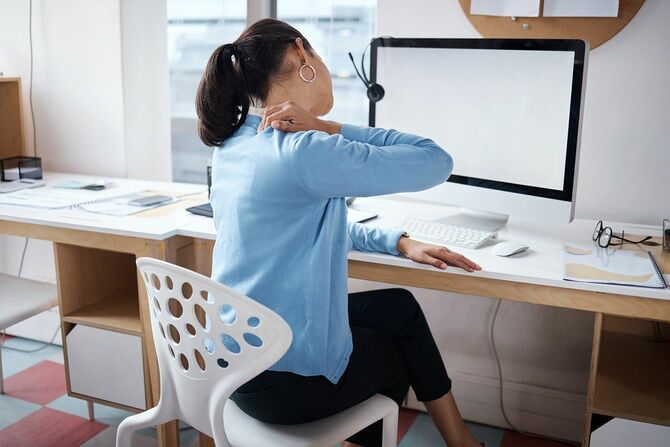 現代のオフィスで彼女の机で働いている間に背中の痛みを経験しているビジネスウーマンのショット