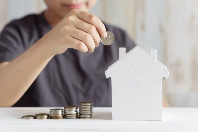 家の形をした貯金箱に100円玉を入れようとしている男の子