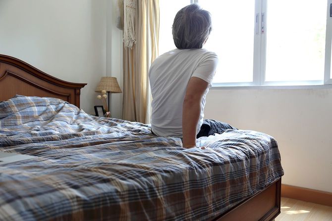 ベッドに座ったまま外を見ている男性