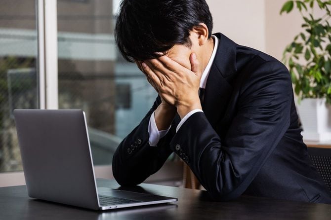 オフィスにて悔し気に顔を覆うビジネスマン