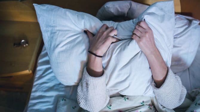 ベッドにあおむけになり枕で顔を覆う女性