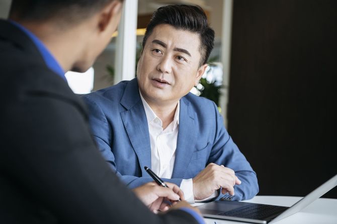 男性の同僚と会話をしている青いジャケットを着た50代の男性