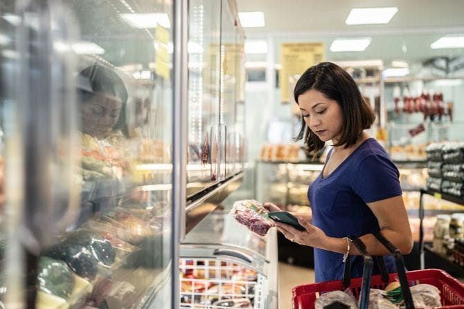 スーパーで肉を手にスマホで調べ物をしている女性