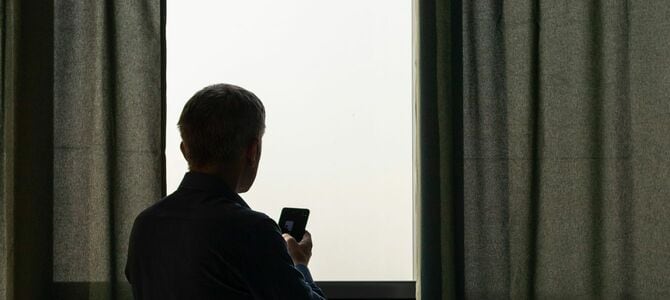 窓際に携帯電話を持った男性のシルエット