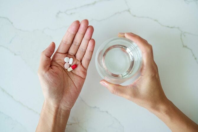 片手の手のひらに薬を乗せ、もう片方の手で水の入ったコップを持つ人
