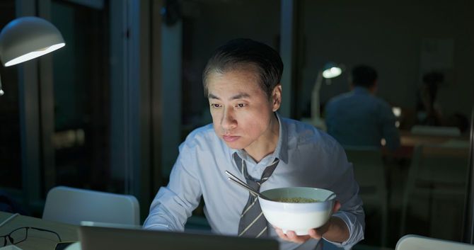 夜間にオフィスでラーメンを食べながら働く男性