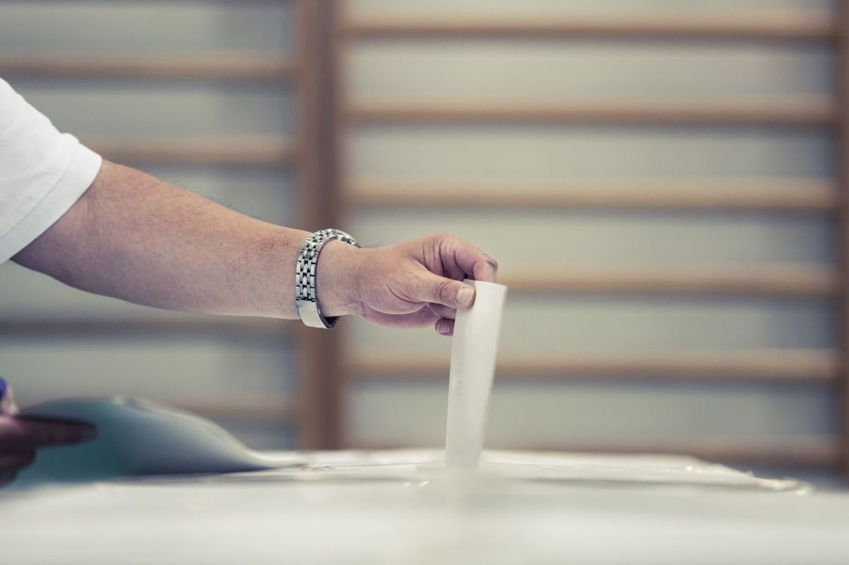 投票所で投票用紙を投じる人の手