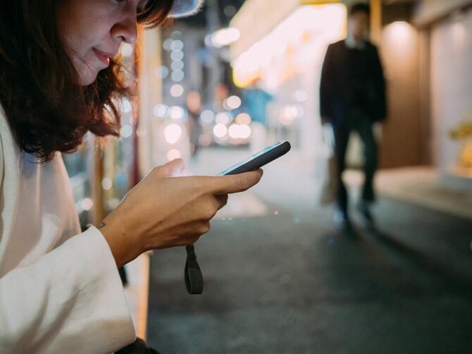 夜の街でスマートフォンを操作する女性