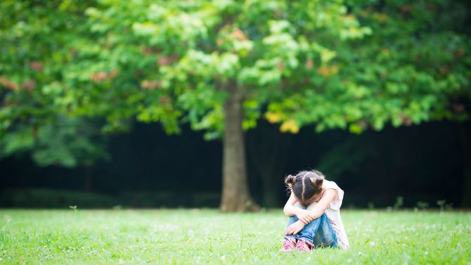 芝生のうえで、ひとり膝を抱えて泣いている少女