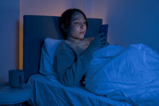 ベッドに入ってスマホを使用している女性