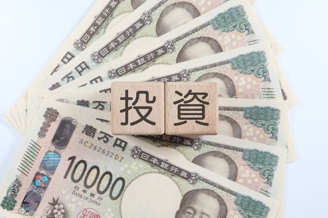 1万円札紙幣と「投資」と描かれた木製ブロック