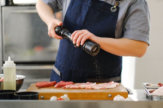 ペッパーミルで肉にコショウをふっている男性