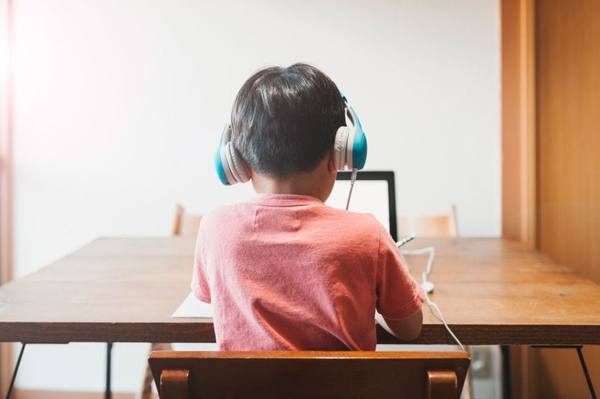 自宅でヘッドセットをつけてオンライン学習をする少年