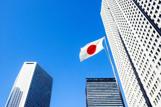 青空にはためく日本の国旗と、西新宿の高層ビル群