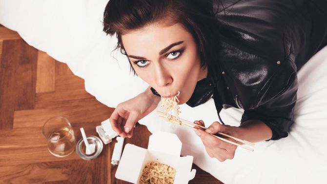 ベッドに寝そべって麺を食べるいたずらな女性