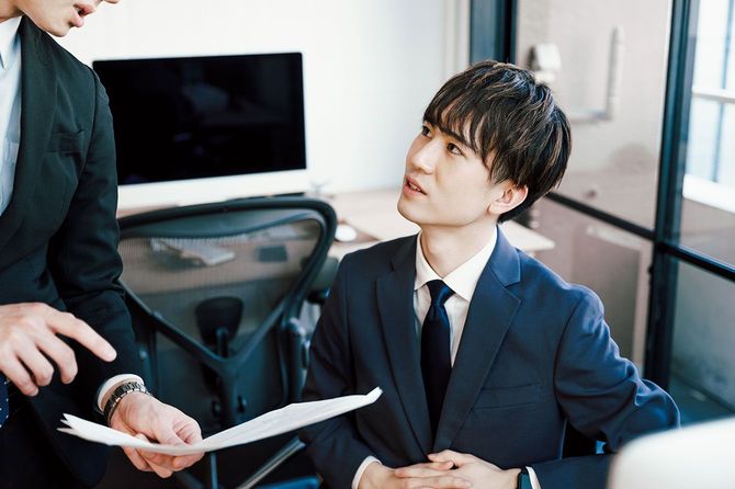 オフィスのデスクで資料を見ながら話をする2人のビジネスマン