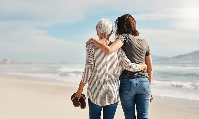 彼女の高齢の母親とビーチに沿って散歩に行く若い女性のリアビューショット