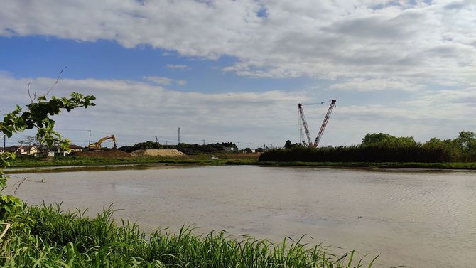 分譲地の道路から、銚子連絡道路の延伸工事現場が見えるが、この分譲地はその延伸予定地には含まれておらず、町が計画する産業用地への転換の予定もない。