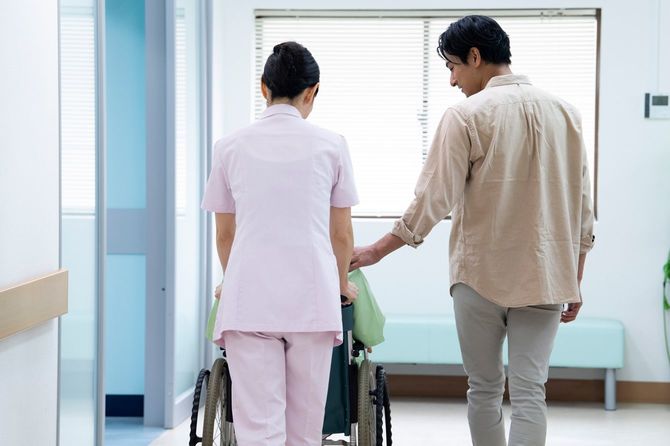 車椅子を押す看護師と一緒に歩く患者の家族の男性