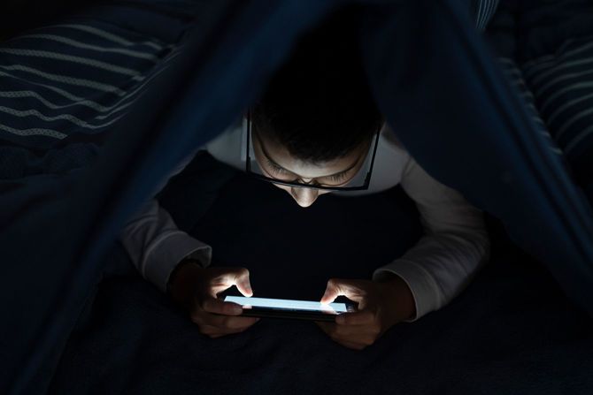 電気を消した暗い部屋のなか、布団をかぶってゲームをしている、眼鏡をかけた少年