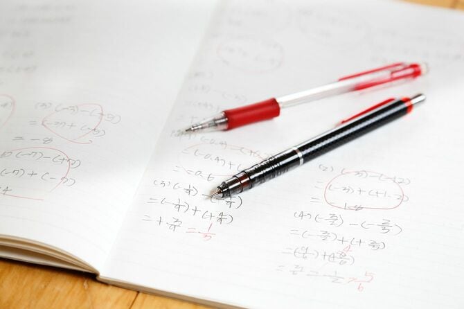 数式が描かれたノートの上に赤ペンとシャープペンシル