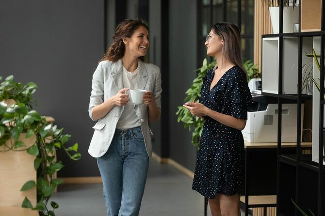 オフィスの廊下でコーヒーを手に立ち話をする2人の女性