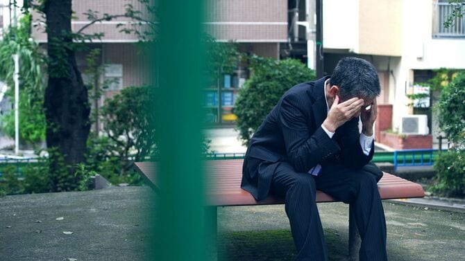 ベンチに座って頭を抱える男性