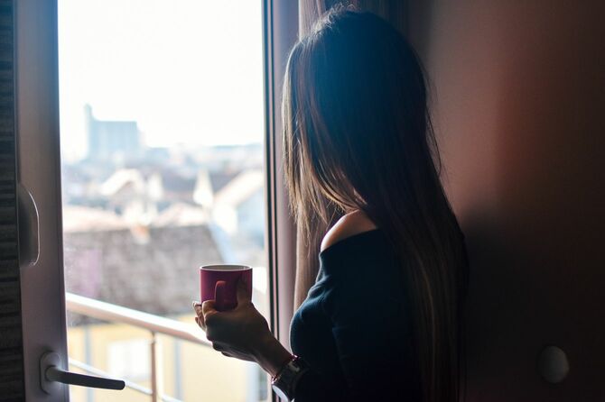 マグカップを手に、窓から外を眺める女性