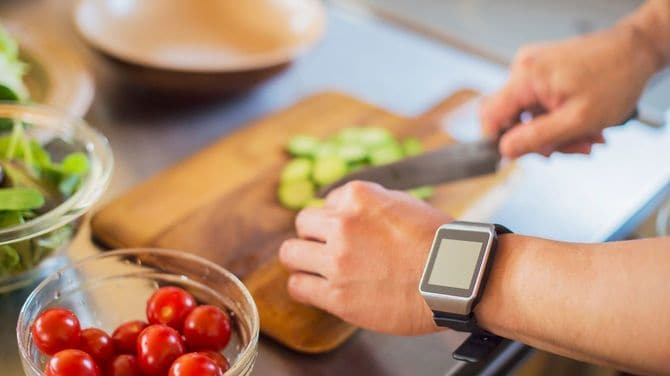 キッチンでスマートウォッチを着けたまま、キュウリを切る男性の手元